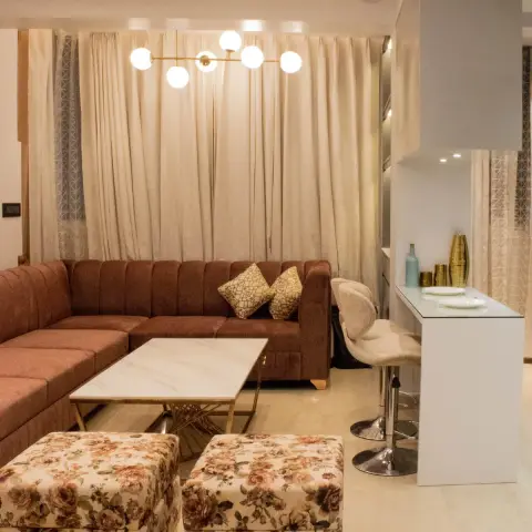A rust-toned channel-tufted sectional sofa with floral ottomans and a marble-and-gold coffee table, beneath a brass sputnik pendant light