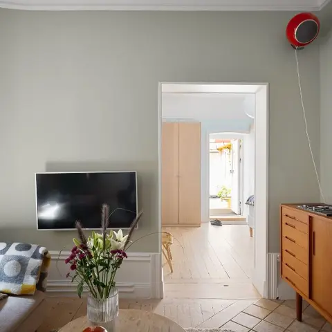 A sage-grey living room with a wall-mounted TV and a mid-century wood sideboard styled with a turntable, doorway open to a hallway beyond.