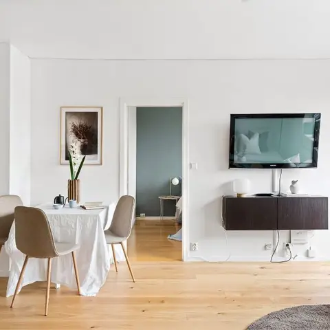 A Scandinavian-style living-dining space with a floating dark-wood TV console, a round dining table dressed in white linen with beige upholstered chairs