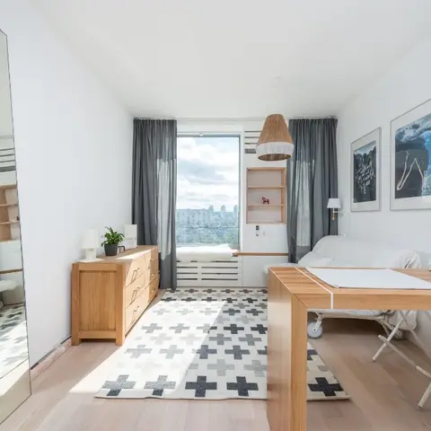 A single pale-oak room combining a placemat-set dining table and a white daybed, with a black-cross-motif rug