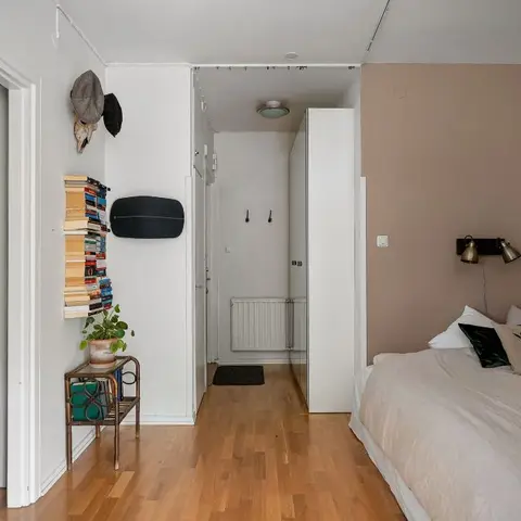 A small studio bedroom with a mauve accent wall behind the bed, twin brass wall-mounted reading lights