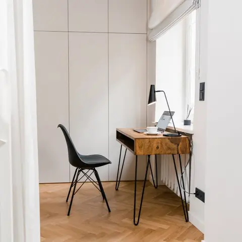 A small study nook with a wood hairpin-leg desk holding a laptop and desk lamp, a black Eames-style chair, a built-in wardrobe wall