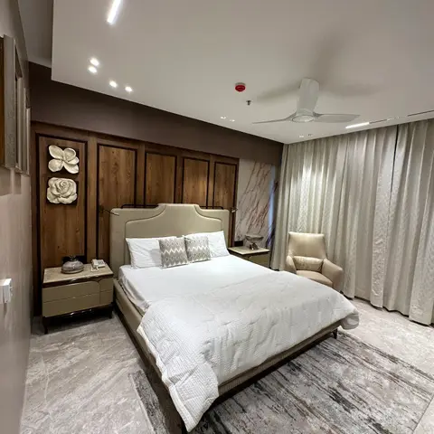 A spacious bedroom with a wood-panelled headboard wall featuring sculptural floral wall art, a tufted cream bed, bedside nightstands
