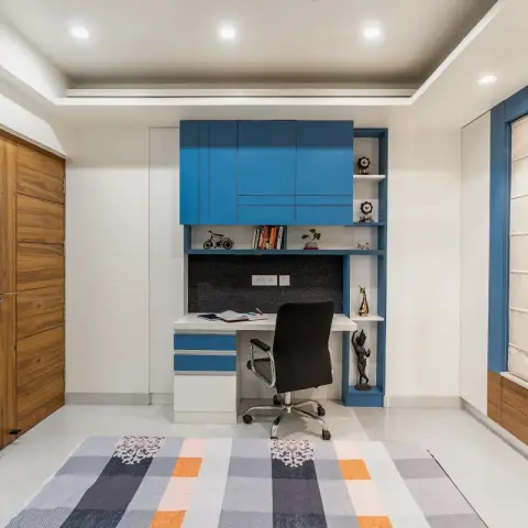 A study nook with a bold blue built-in desk unit, overhead cabinets and open display shelving, paired with a striped area rug.