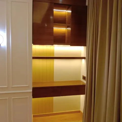 A study nook with a floating wood desk and drawers, a backlit fluted panel accent wall, and a dark wood overhead cabinet with warm interior lighting