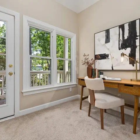 A study nook with a mid-century wood desk with rattan drawer fronts, a cream upholstered chair, and a large abstract black-and-white artwork above.