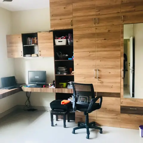 A study nook with a wood-laminate wraparound desk holding a computer and laptop beneath open bookshelves