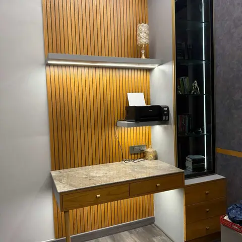 A study nook with fluted wood wall panelling, a floating marble-top desk with drawers, and a backlit glass display cabinet.
