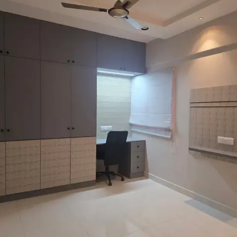 A study room with full-height grey wardrobes with textured lower panels, a built-in study desk and chair by the window