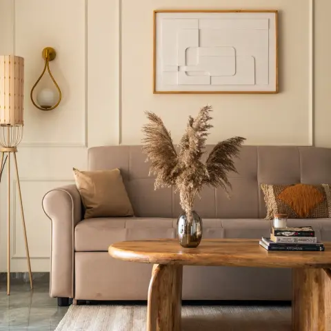 A taupe roll-arm sofa against a cream moulded wall, with a white relief artwork in a teak frame above it