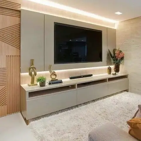A taupe TV console wall with a warm backlit panel, a geometric carved-wood sliding door, and a plush cream shag rug in front.