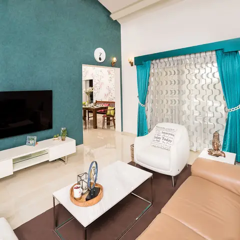 A teal textured accent wall behind the TV pairs with a tan leather sofa and teal drapes with sheer embroidered curtains