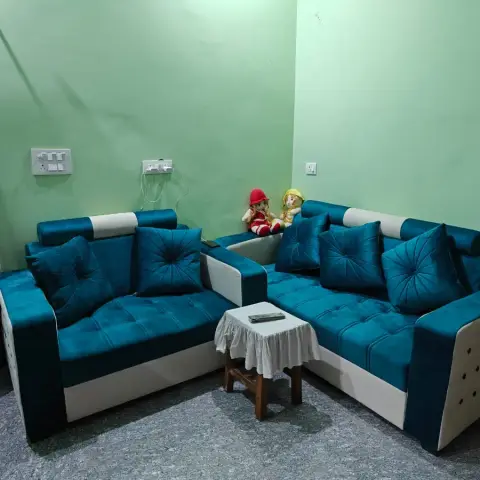 A teal velvet L-shaped sofa set against mint-green walls, with a cloth-covered wooden stool used as a side table on a speckled stone floor.