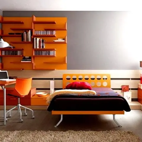 A teen bedroom with a vivid orange fitted bed with a circle-cutout headboard panel, a matching wall-mounted bookshelf, a study desk with a task lamp