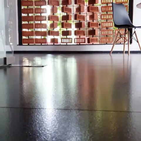 A terracotta brick jaali screen filters daylight and greenery into an entrance area with a single black shell chair and reflective dark flooring.