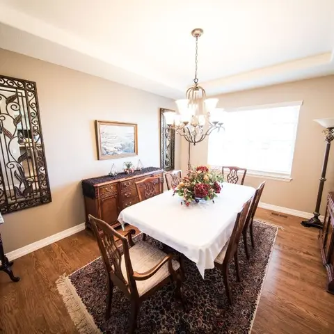 A traditional dining room with a wood table set under a wrought-iron framed mirror and a candle chandelier, beside a glass-front china cabinet.