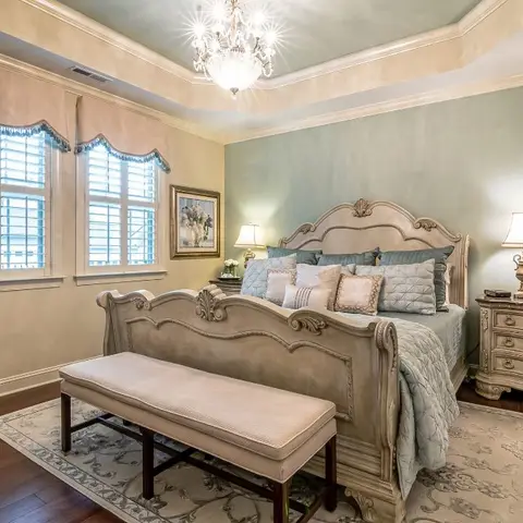 A traditional master bedroom with a carved wood sleigh bed, matching bedside dressers, a crystal chandelier under a tray ceiling