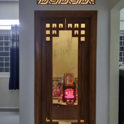 A traditional wooden pooja room with a carved jaali door fitted with brass bells, a geometric jaali transom
