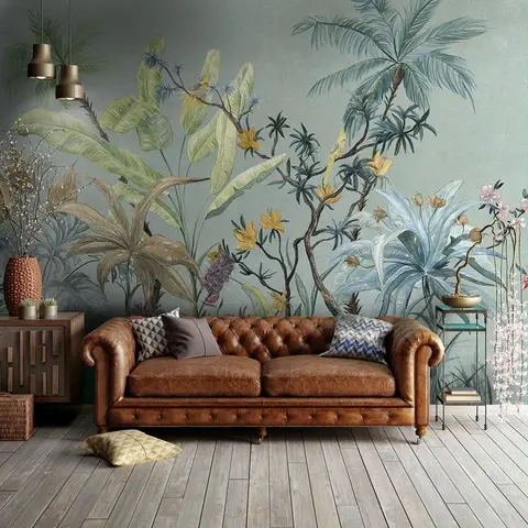 A tufted brown leather chesterfield sofa sits on a wood-plank floor in front of a floor-to-ceiling botanical mural wallpaper of palms and tropical birds.
