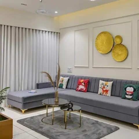 A tufted grey L-shaped sofa with playful animal-print cushions sits below a gold sunburst-disc wall sculpture, framed by a rectangular linear LED ceiling light.