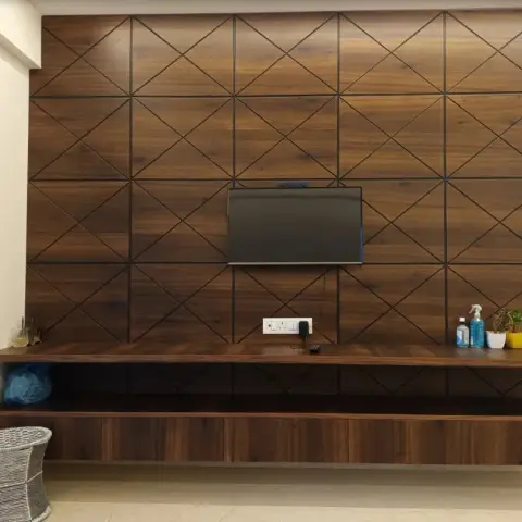 A TV feature wall clad in wood panelling with a diagonal cross-lattice groove pattern, above a floating wood console styled with small potted plants