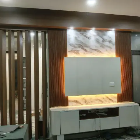 A TV wall under construction with a backlit marble-clad panel flanked by fluted wood pilasters, beside a slatted wood partition screen