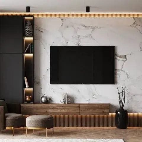 A wall-hung TV on a book-matched white marble panel, flanked on one side by matt black cabinetry with a lit vertical niche column and on the other by