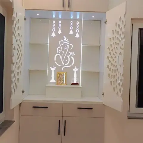 A wall-mounted pooja unit with laser-cut jaali cabinet doors opening to a backlit Ganesha motif and shelved idols.