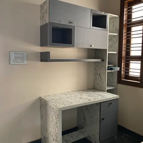 A wall-mounted study desk with marble-laminate top and grey overhead storage cubbies, photographed corner-on near a window.