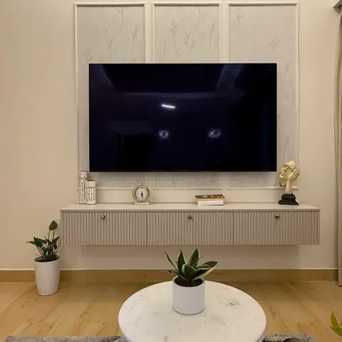 A wall-mounted TV framed by fluted moulding panels above a floating ribbed console with a round marble-top coffee table in front