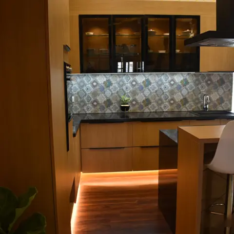 A warm wood-toned kitchen with a patterned tile backsplash, black stone counter, a glass-front display cabinet