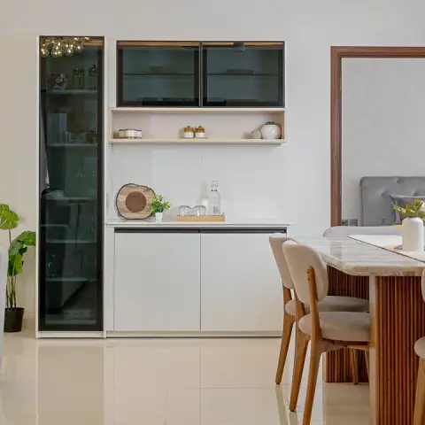 A white crockery unit with a tall smoked-glass display column and a slim oak open shelf stands beside a fluted-pedestal dining table with a marble top
