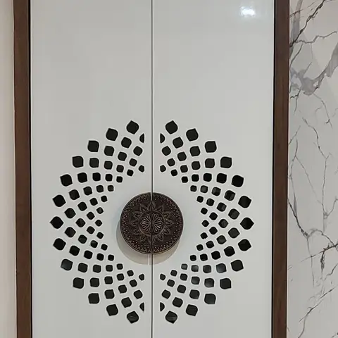 A white lacquered pooja cabinet with a laser-cut mandala jaali pattern and antique copper door pull