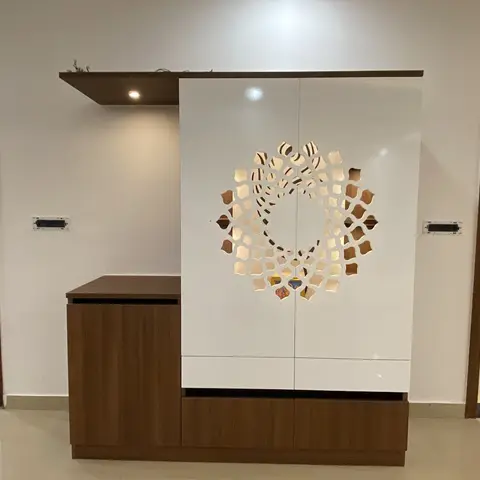 A white lacquered pooja cabinet with a backlit laser-cut mandala medallion, paired with a walnut console, in an entryway opening to other rooms.