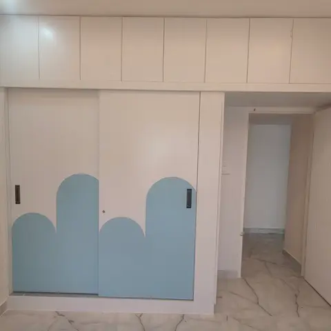 A white loft wardrobe with sky-blue cloud-shaped cutout sliding doors in a child's bedroom, opening to a marble-floored hallway.