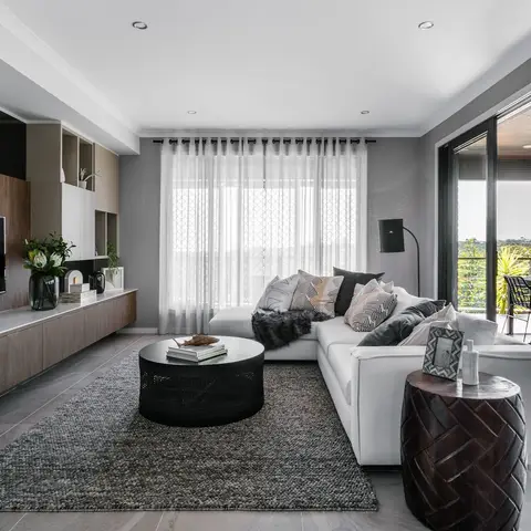A white sectional sofa with a round black coffee table on a grey rug faces a dark wood TV console
