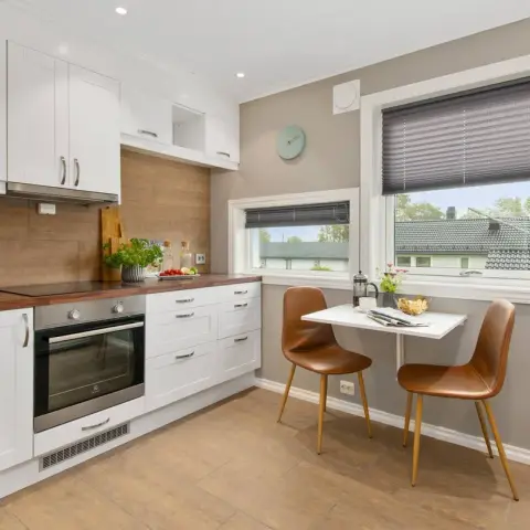A white shaker kitchen with a walnut butcher-block counter and a small two-seat breakfast table tucked into the window corner.