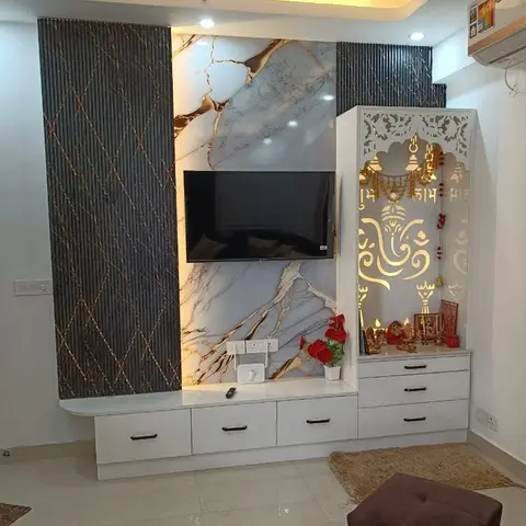 A white TV console with book-matched marble backsplash and fluted dark panelling sits beside a jaali-cut pooja niche with Ganesh motif