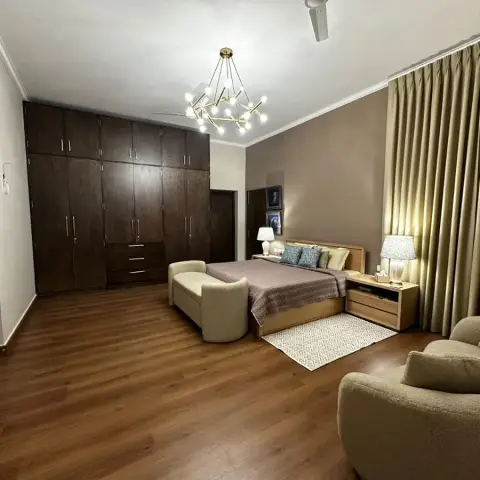 A wide bedroom where a dark-stained six-door wardrobe faces a light oak bed, with a brass sputnik chandelier