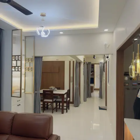 A wide open-plan view from a brown leather sofa through a dining table set to a hallway leading to a bedroom