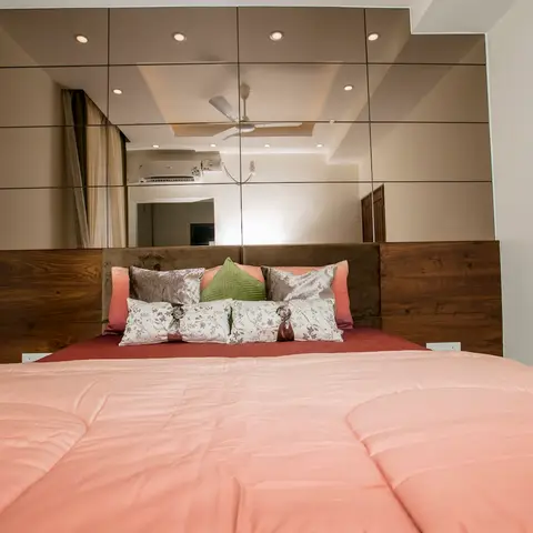 A wood-and-upholstered headboard bed with coral bedding, set beneath a full mirrored panel wall that reflects the ceiling and fan.