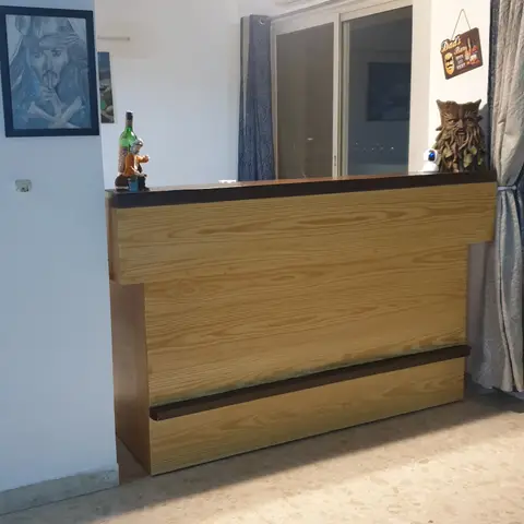 A wood-panelled home bar counter tucked into the corner of a living room, styled with framed art and novelty decor pieces.