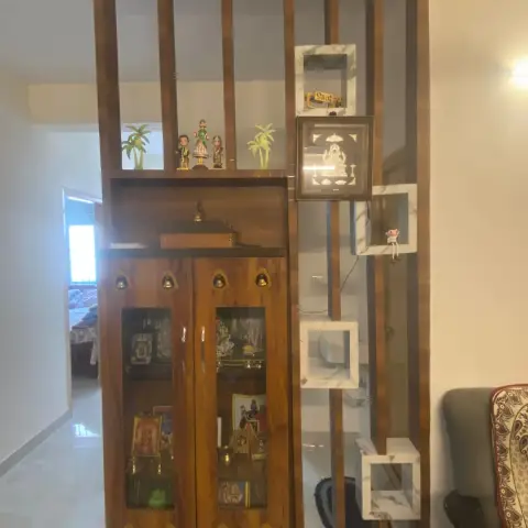 A wood pooja cabinet with brass bells and glass doors beside a slatted wood room-divider fitted with marble-inset display cubes.