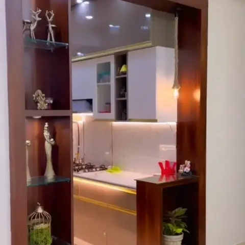 A wood-veneer entrance partition with glass-shelved curio display opens onto a marble-backsplash kitchen with gold-trimmed cabinetry beyond.