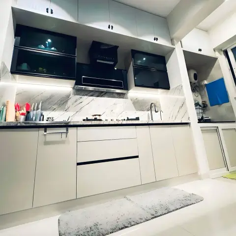 A working kitchen in white handleless shutters with a black granite counter and a grey-veined marble backsplash