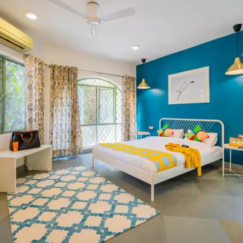 Airy bedroom with a peacock-teal accent wall, a white wire-framed bed under twin brass cone pendants