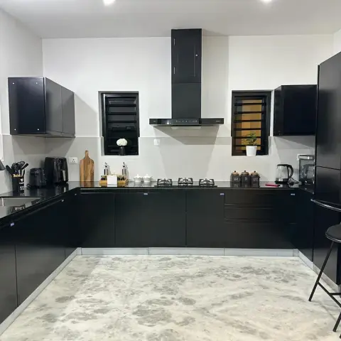 All-black U-shaped kitchen with matte black cabinetry, a black chimney hood, black granite countertops, black window grilles, and bar seating along one edge.