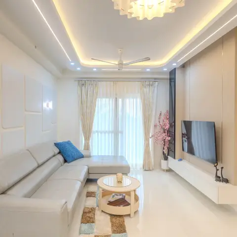 All-cream living room where a routed grid of slim wall mouldings runs behind a pale leather L-sofa with one blue checked cushion