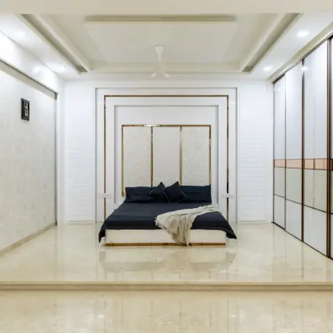 All-white bedroom on a raised marble platform, the low bed recessed into layered fluted panels framed by gold trims