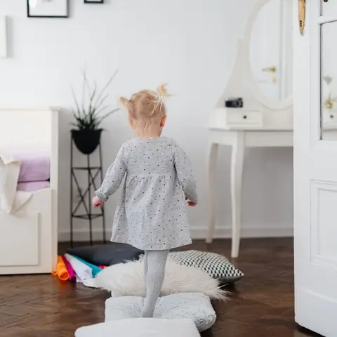 All-white child's room seen through a glazed panel door: beadboard daybed with a pull-out drawer base and lilac bedding